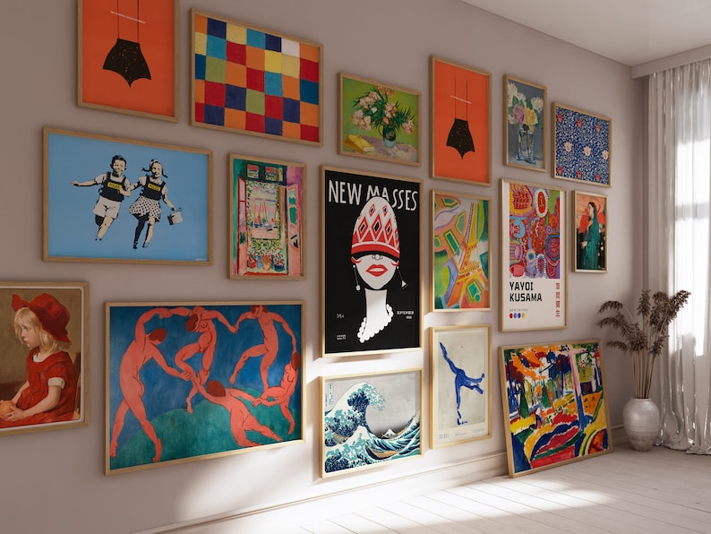 May include: A collection of framed art prints displayed on a wall. The artwork includes various styles, such as abstract, figurative, and graphic designs. The frames are a light brown color, and the art pieces are of different sizes and shapes.