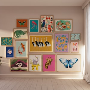 May include: A collection of framed art prints featuring various animal and nature-themed illustrations. The artwork includes images of butterflies, cats, flamingos, koi fish, and giraffes. The prints are displayed on a neutral wall with a potted plant.
