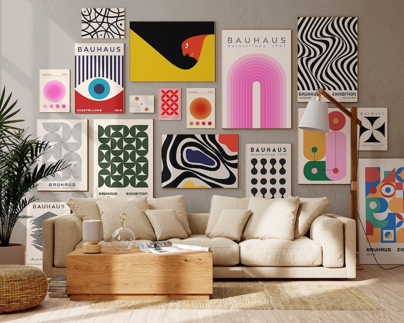 May include: A living room interior with a beige sofa and a wooden coffee table. The wall is decorated with a collection of colourful geometric and abstract Bauhaus art prints. The prints feature various shapes, patterns, and colours, including black, white, red, yellow, green, blue, and pink. The prints are arranged in a grid pattern on the wall.
