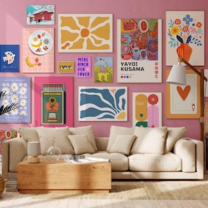 May include: A collection of framed art prints in various sizes and styles, including floral, abstract, and geometric designs. The prints are displayed on a pink wall above a beige sofa and wooden coffee table. A floor lamp and a potted plant are also visible.