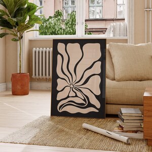 May include: A black framed print of a large, abstract flower with a beige background. The flower has a stylized, organic shape with rounded edges.