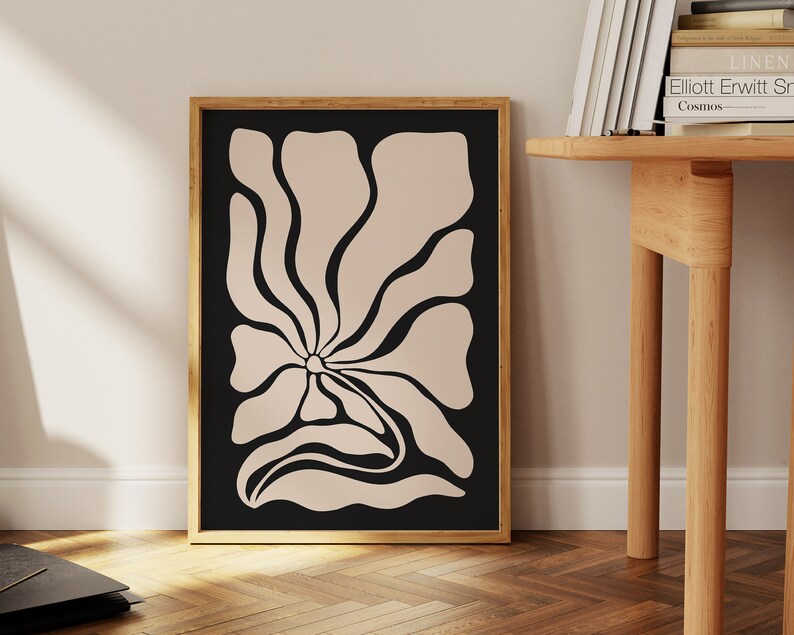 May include: A framed print of a stylized flower with a beige outline on a black background.