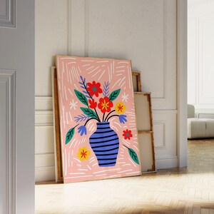 Puede incluir: Un fondo abstracto rosa y blanco con un jarr&oacute;n azul y blanco a rayas lleno de flores coloridas. Las flores son rojas, amarillas y naranjas. El jarr&oacute;n est&aacute; sobre una superficie blanca.