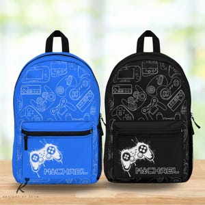 May include: Two backpacks, one blue and one black, featuring a pattern of white video game controllers and consoles. Each backpack has a front pocket with a white controller graphic and the name "MICHAEL". The backpacks have black zippers and handles.