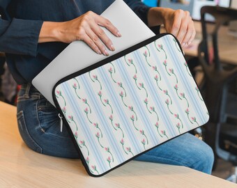 May include: A laptop sleeve featuring a floral pattern with pink rosebuds and green stems against a backdrop of vertical light blue stripes on a white background. The sleeve has a black border and a zipper closure.