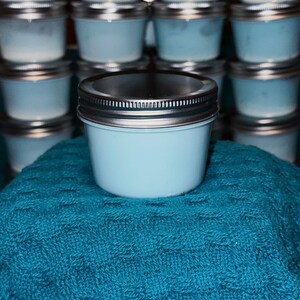 May include: A small, light blue glass jar with a silver lid. The jar is sitting on a blue towel.