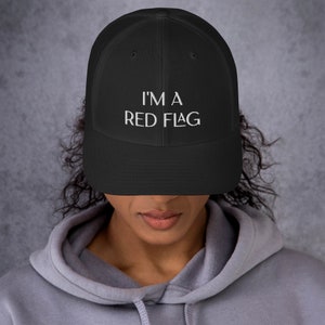 Könnte beinhalten: Eine schwarze Mesh-Trucker-Kappe mit einem weißen gestickten Design, das "I'm a Red Flag" sagt.