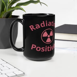 May include: Black ceramic mug with a pink radiation symbol and the text "Radiating Positivity" printed on it.