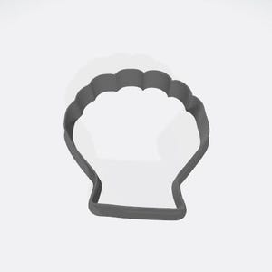 May include: A gray metal seashell cookie cutter. The cutter has a scalloped top edge and a rectangular base. The seashell shape is a popular design for baking cookies and other treats. The cutter is shown against a white background.