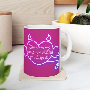 May include: White ceramic mug with a pink gradient background. The mug features a white heart design with devil horns, wings, and the text "You stole my heart, but I'll let you keep it."