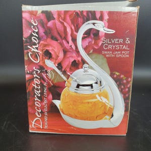 May include: A silver and crystal swan jam pot with spoon. The pot is filled with a golden-colored jam. The packaging reads "Decorators Choice" and "Designed for Elegant Living by Lisa."