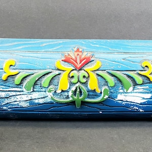 May include: A decorative rolling pin with a blue wooden barrel design. The barrel features a distressed wood grain pattern and is adorned with colorful floral accents in red, yellow, and green. The handles are blue.