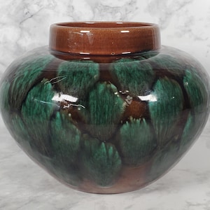 May include: A decorative ceramic vase with a rounded body and a brown rim. The vase features a glossy, textured glaze in shades of green and brown, creating a unique, organic pattern. The vase is a stylish home decor item.