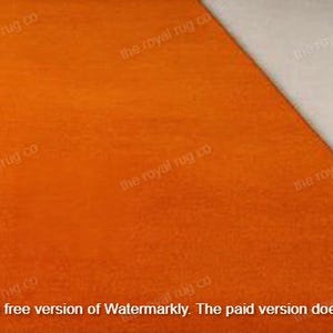 May include: An orange rug with a textured surface, set at an angle against a neutral, off-white surface. The rug's color is a vibrant, solid orange. The text "the royal rug co" is visible in the image.