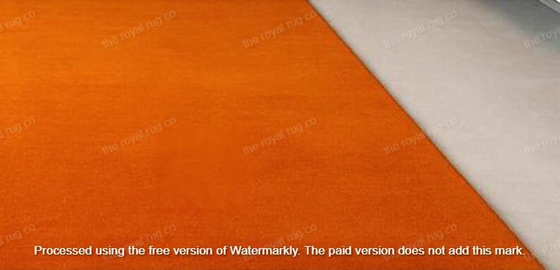 May include: An orange rug with a textured surface, set at an angle against a neutral, off-white surface. The rug's color is a vibrant, solid orange. The text "the royal rug co" is visible in the image.