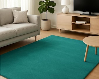 Puede incluir: Una alfombra rectangular de color verde azulado en un salón. La alfombra está colocada sobre un suelo de madera, con un sofá gris, un mueble de madera, un televisor y una pequeña mesa redonda en el fondo. También se ve una planta en maceta.