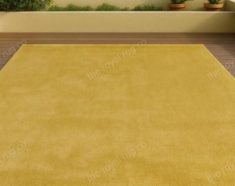 May include: A large, rectangular, mustard-yellow rug. The rug is placed on a wooden deck, with a view of the ocean and potted plants in the background. The rug has a soft, plush appearance.