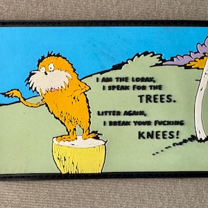 May include: A framed image featuring the Lorax character from Dr. Seuss's book. The Lorax, with orange fur and a white beard, stands on a yellow stump. Text reads, "I AM THE LORAX, I SPEAK FOR THE TREES. LITTER AGAIN, I BREAK YOUR FUCKING KNEES!"