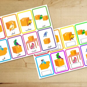 May include: A set of colourful flashcards with images of birds and boxes. Each card has an Arabic word written on it. The words are: "Khlf", "Amam", "Rajalb", "Namt", "Fawq", "Ala", "Fi", "Bin".