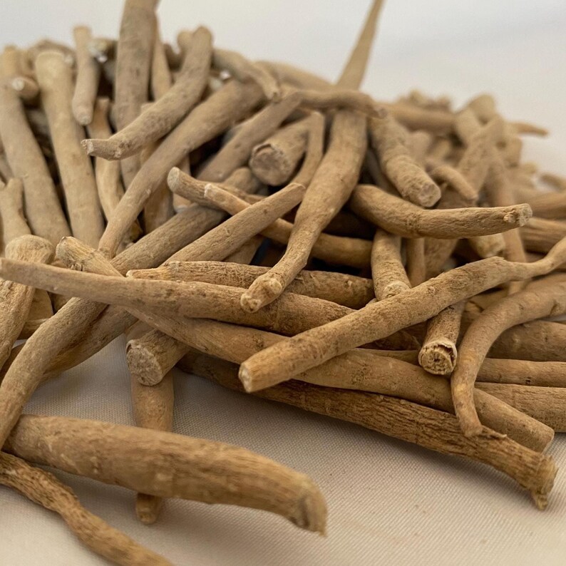 May include: A pile of dried, tan-colored ashwagandha roots. The roots are cylindrical, with a rough texture and varying lengths. The image is a close-up, showing the details of the roots.