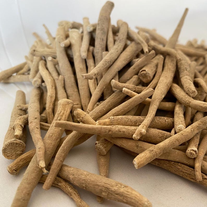 May include: A close-up shot of a pile of dried, light brown ashwagandha roots. The roots are cylindrical, with varying lengths and thicknesses. The image is well-lit, highlighting the texture and natural color of the roots.