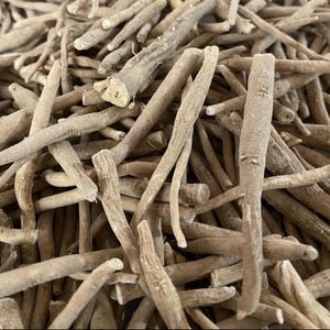 May include: Close-up of a pile of dried, light brown ashwagandha roots. The roots vary in size and shape, with a rough, textured appearance. The image is well-lit, highlighting the natural color and details of the herbal product.