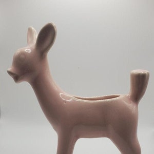 Puede incluir: Una figurita de ciervo de cerámica rosa con la espalda hueca, ideal para guardar pequeñas plantas u otros objetos decorativos.