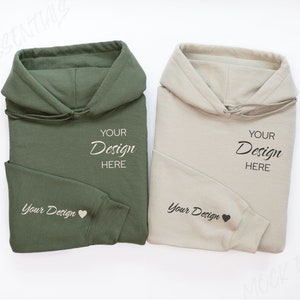 Könnte beinhalten: Zwei gefaltete Hoodies, einer grün und einer beige, mit dem Text "Your Design Here" auf jedem. Beide Hoodies haben ein kleines Herzdesign auf dem Ärmel.