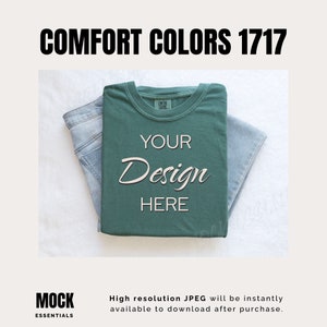 May include: A folded green t-shirt with the text "YOUR Design HERE" on it. The t-shirt is on top of a pair of blue jeans. The background is white.