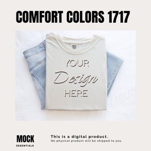 May include: A white t-shirt with the text "YOUR Design HERE" on it. The t-shirt is folded and laid on a white surface with a pair of blue jeans folded next to it.