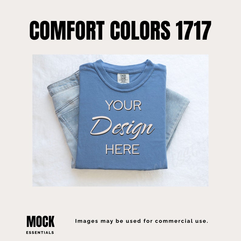 May include: A folded blue t-shirt with the text "YOUR Design HERE" on the front. The t-shirt is on a white surface with a pair of blue jeans folded on top of it.