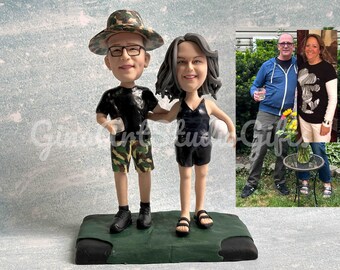 May include: A custom-made figurine set of a couple, the man wearing a camouflage hat, black shirt, and camouflage shorts, and the woman wearing a black tank top and black shorts. The figurines are standing on a green base. The couple is holding a small white ball.