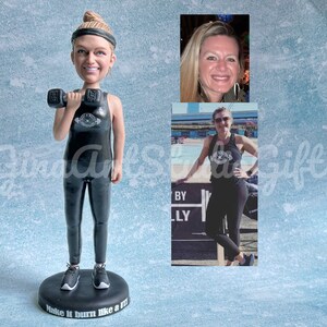 May include: A black and white custom bobblehead figurine of a person wearing a black tank top with a white logo and black leggings. The person is holding a black dumbbell in their right hand. The bobblehead is standing on a black base with the text "Make it burn like a m**" printed on it.