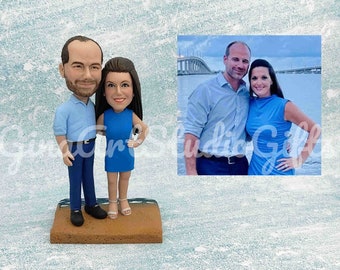 May include: A custom-made figurine set of a couple, the man is wearing a blue shirt and blue trousers, the woman is wearing a blue dress, they are standing on a brown base.
