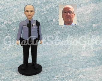 May include: A custom figurine of a person wearing a blue uniform with a black tie and a badge. The figurine is standing with its hands on its hips. The person's face is visible in the image. The figurine is on a black base.