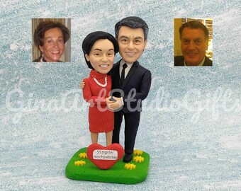 May include: A custom-made figurine of a couple standing together. The woman is wearing a red dress and the man is wearing a black suit. They are standing on a green base with a red heart that says "55zigster Hochzeitstag".