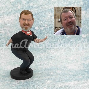 May include: A custom bobblehead figurine of a person with a beard wearing a black shirt and red scarf. The figurine is standing on a black base. A photo of the person is shown in the background.