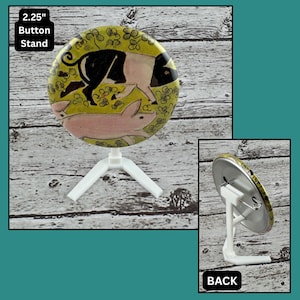 May include: A 5.7 cm button featuring a pig illustration, mounted on a white stand. The button shows a black and white pig and a pink pig on a yellow background with floral details. The word "BACK" is visible.