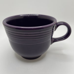 May include: A purple ceramic mug with a rounded shape and a handle. The mug has a ribbed design.