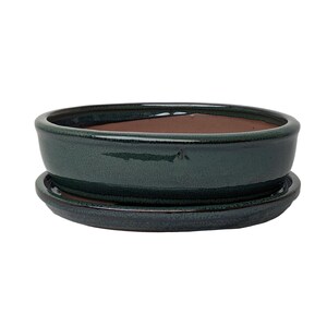 May include: A dark green glazed oval ceramic bonsai pot with a matching saucer. The pot has a slightly raised rim and a smooth, glossy finish.