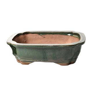 May include: A rectangular green glazed ceramic bonsai pot with a brown clay interior. The pot has a slightly flared rim and four small feet.