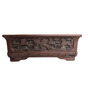 May include: A rectangular brown ceramic planter with a raised design of horses running in a line. The planter has a decorative border and three legs.