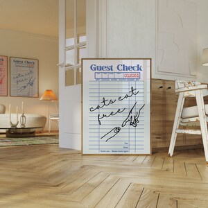 K&ouml;nnte beinhalten: Ein wei&szlig;er gerahmter Druck mit einem blauen und schwarzen Design auf einem G&auml;stecheck. Der Text auf dem Druck lautet "Guest Check 012051" und "cats eat free".