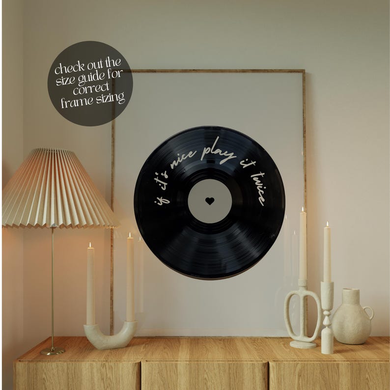 May include: A framed print featuring a black vinyl record design with the text "if it's nice play it twice" in white script. The print is displayed above a wooden cabinet, with a lamp and candles. The text "check out the size guide for correct frame sizing" is also visible.
