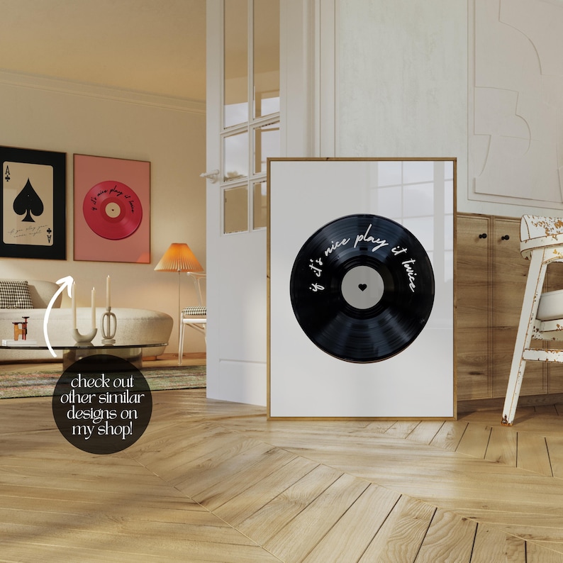 May include: A framed print featuring a black vinyl record with the text "if it's nice play it twice" in white script. The record has a white center with a heart. Other framed art pieces are visible in the background.