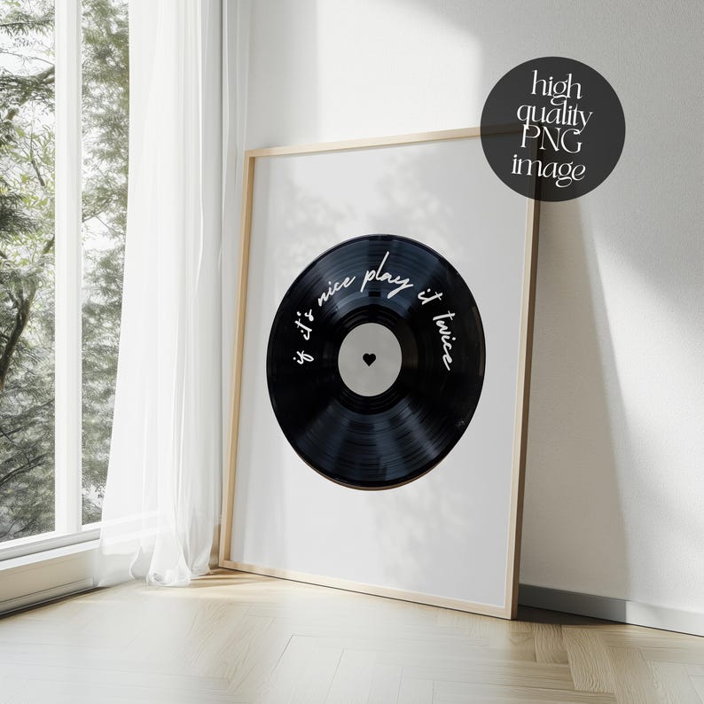 May include: A framed print featuring a black vinyl record design. The record has the text "if it's nice play it twice" in white script. The print is in a light wood frame and is leaning against a wall near a window.