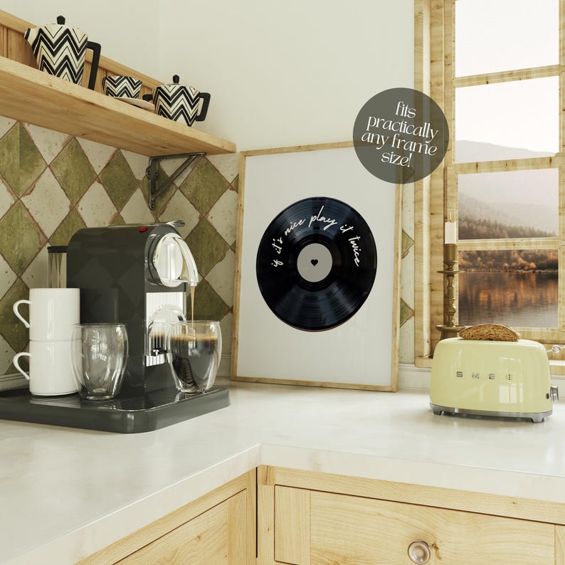 May include: A kitchen scene with a black espresso machine, white mugs, and clear glasses. A framed print of a vinyl record with the text "If it's nice play it twice" hangs on the wall. A yellow toaster sits on the counter.