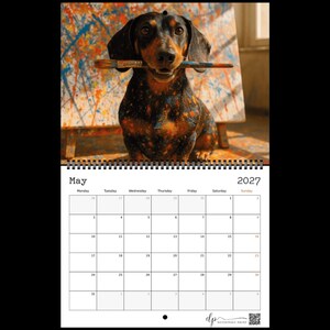 May include: A 2027 wall calendar for the month of May featuring a black and tan dachshund covered in colorful paint splatters, holding a paintbrush in its mouth in front of an easel with a paint-splattered canvas. The calendar grid is white.