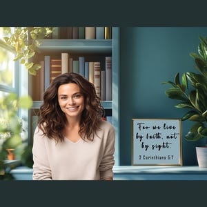 May include: A woman with long brown hair smiles at the camera. She is standing in front of a bookshelf with a quote on the wall that reads "For we live by faith, not by sight. 2 Corinthians 5:7".