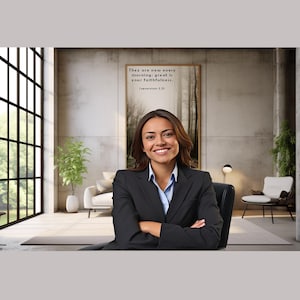 May include: A woman in a black blazer sits in a chair in a modern office setting. She is smiling and has her arms crossed. Behind her is a large window with a view of trees. A framed print with the text "They are new every morning; great is your faithfulness." is on the wall.